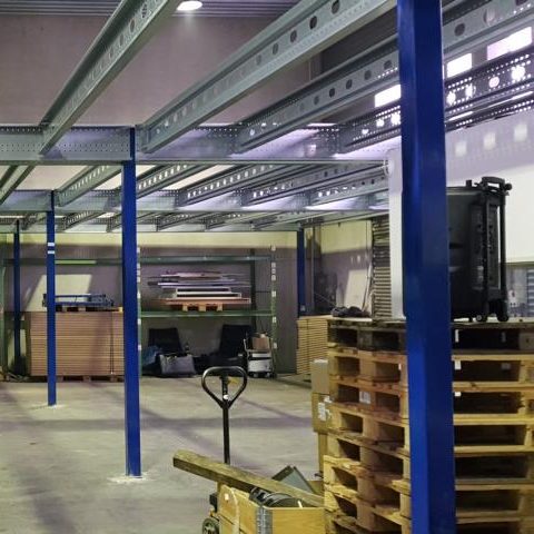 Lagerraum mit Regalen, Paletten und einem Handwagen, gut beleuchtet.