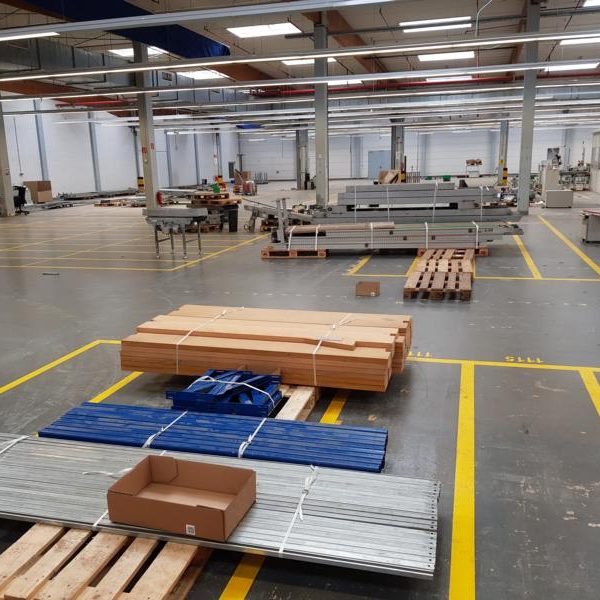 Lagerhalle mit Holz- und Metallmaterialien, leeren Paletten und Maschinen.