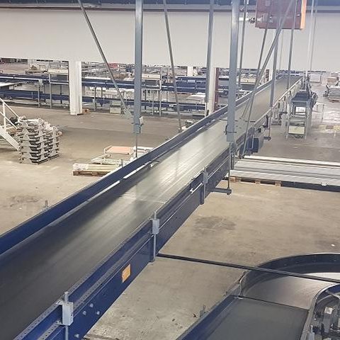 Förderband in einer Lagerhalle mit drehbarem Kranausleger im Hintergrund.