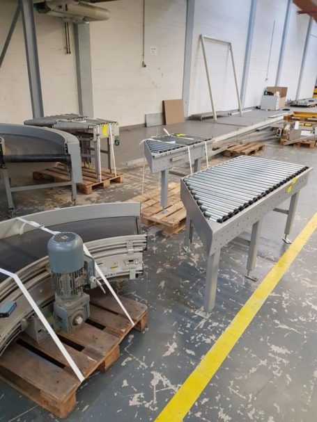 Förderbandanlage in einer Lagerhalle, strukturierte Metalloberflächen und Elektromotor sichtbar.