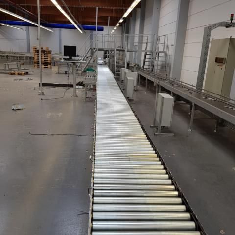 Leerer Förderband in einer Industriehalle mit Metallgestrüpp im Hintergrund.