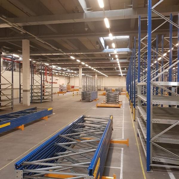 Leere Lagerhalle mit blauen Regalsystemen und Metallgestellen.
