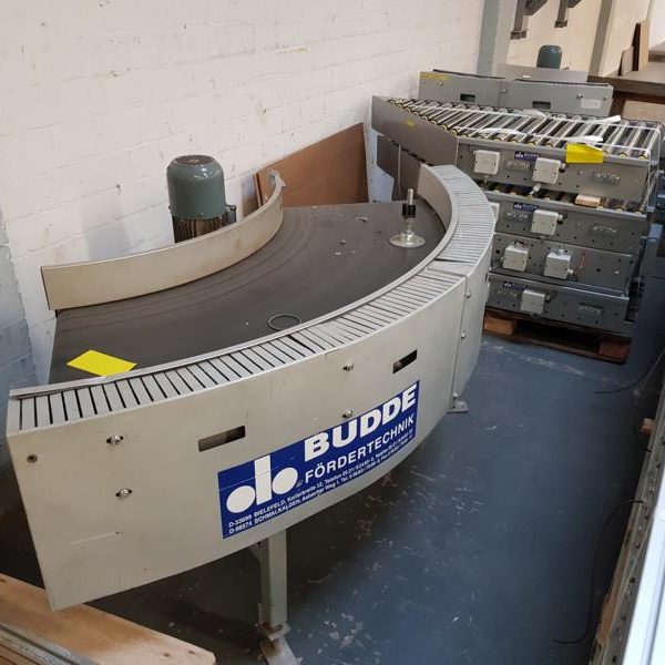 Bogenförmiger Förderband mit Lagereinheiten im Hintergrund auf dem Boden.