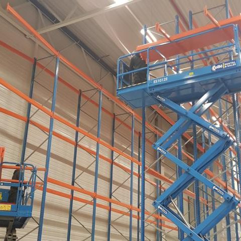 Blaue Regalanlage mit orangefarbenen Elementen und Arbeitsbühne in einem Lager.