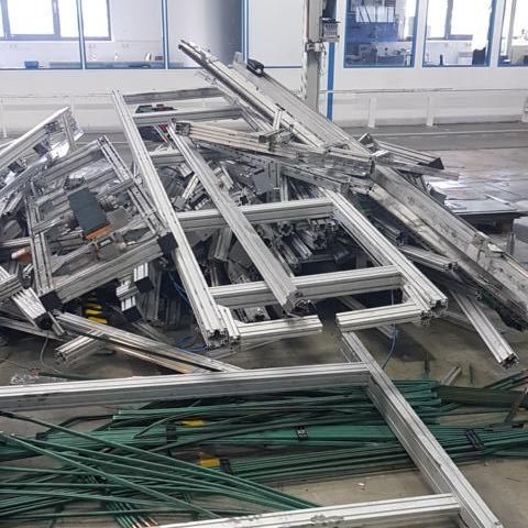 Ein Haufen von Aluminiumrahmen und Gerüstteilen auf dem Boden eines Fabrikgebäudes.